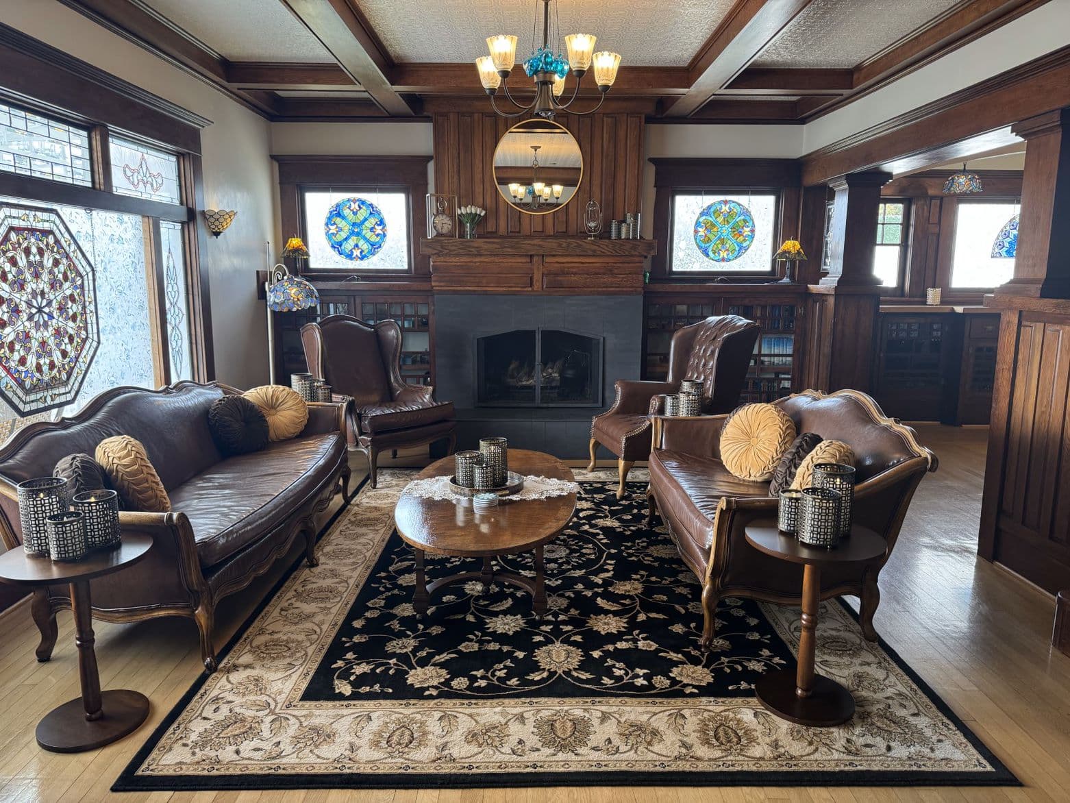 A cozy, elegantly designed living room featuring leather furniture, stained glass windows, and a stone fireplace.