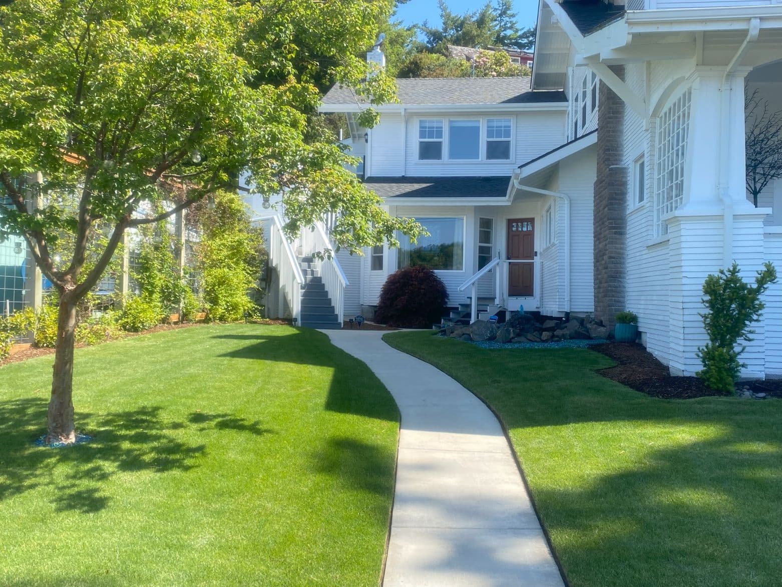A well-maintained lawn leading to a two-story white house with a wooden front door and surrounding greenery.