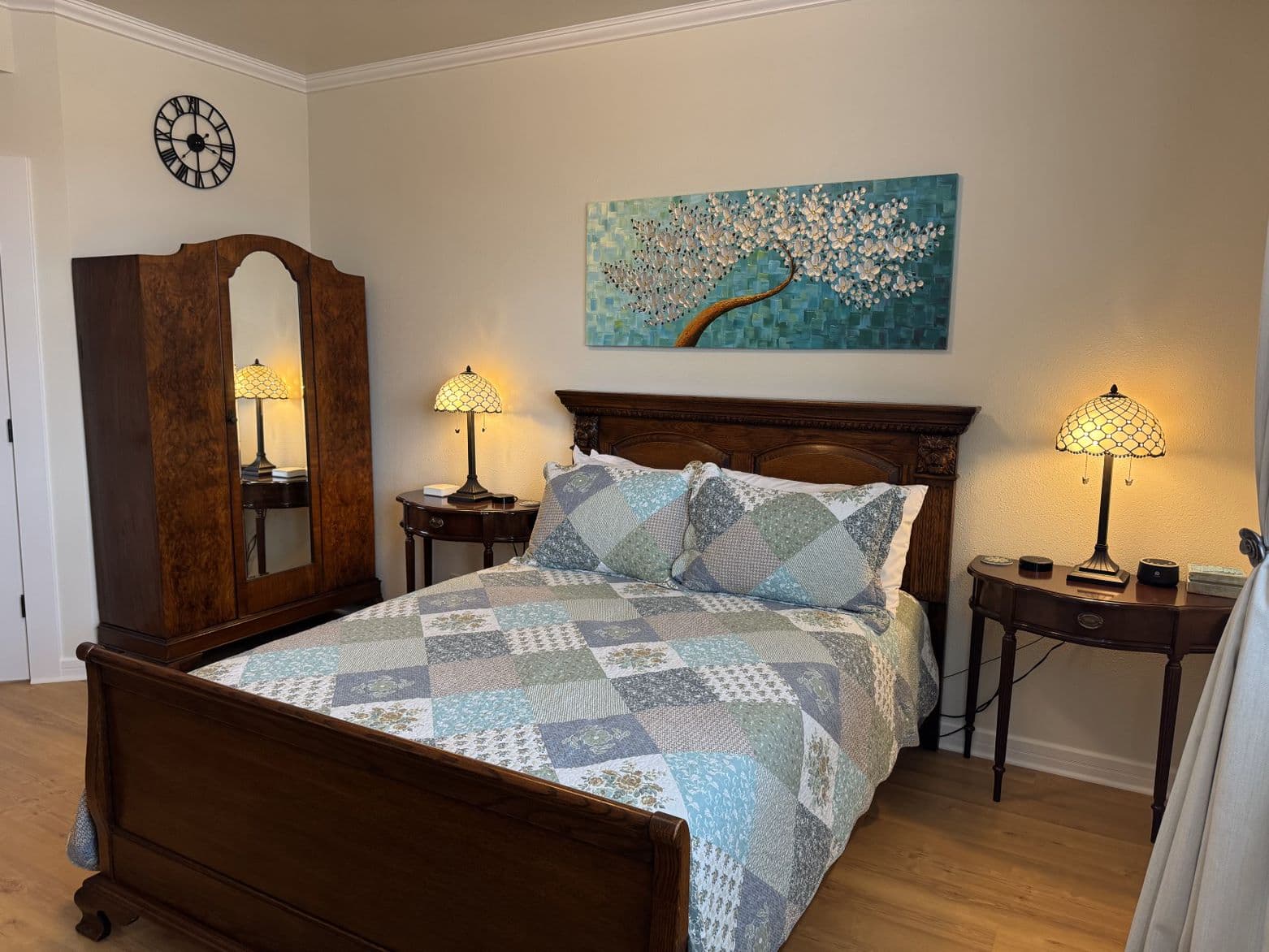 A cozy bedroom featuring a wooden bed with a patchwork quilt, bedside tables with lamps, and a tall wardrobe.